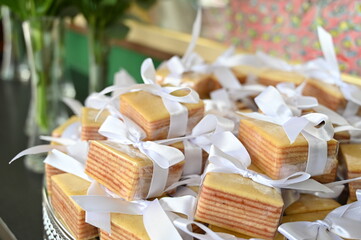 Traditional Brazilian Bem-Casado wedding favors with lilac ribbons, elegant sweets display on acrylic stand for reception, close up of tiered sponge cake treats with floral background