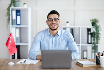 Fototapeta premium Portrait of millennial male teacher with laptop teaching Turkish online from home, smiling at camera. Confident Arab male tutor conducting educational web conference or webinar