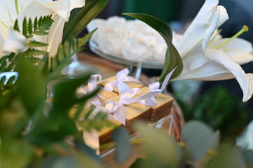 Traditional Brazilian Bem-Casado wedding favors with lilac ribbons, elegant sweets display on acrylic stand for reception, close up of tiered sponge cake treats with floral background