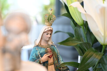 Statue of Our Lady with sacred heart and golden crown, religious Catholic figure for wedding altar decoration, close up of Virgin Mary icon with white lily flower in the foreground