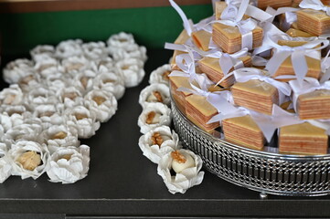 Traditional Brazilian Bem-Casado wedding favors with lilac ribbons, elegant sweets display on acrylic stand for reception, close up of tiered sponge cake treats with floral background