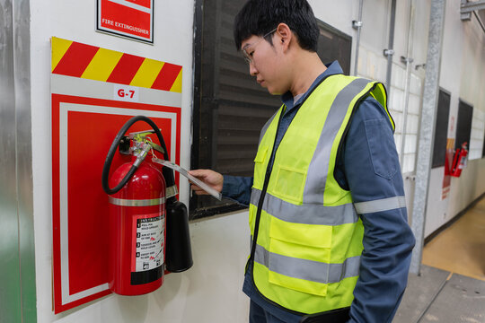 technician in safety vest inspecting fire extinguisher in industrial building, checking equipment for workplace fire safety compliance, maintenance, and emergency preparedness.