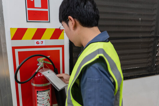 Safety technician inspects fire extinguisher in industrial facility, checking inspection tag and readiness to ensure emergency response compliance and workplace fire safety.