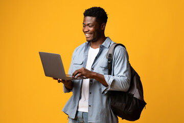 Smiling african american male student positive guy in casual with backpack using modern laptop on...