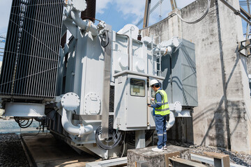 Naklejka premium Electrical technician inspecting power transformer control cabinet at substation, checking operational data, equipment condition, safety status, and system reliability during routine maintenance.