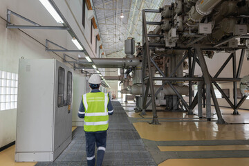 Engineer walking through an indoor power facility, observing electrical equipment and infrastructure, supporting inspection routines, safety awareness, and preventive maintenance in industrial energy.