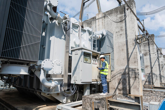 Power engineer performing transformer inspection at outdoor high voltage substation, checking control cabinet status, operational parameters, maintenance records, and electrical system performance.