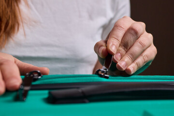 Traveler opening luggage, Close shot of hands unfastening suitcase zipper before travel, Detailed view of hands pulling zipper on vibrant teal travel case with anticipation