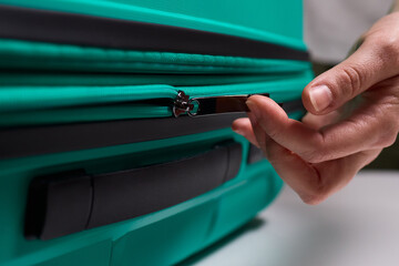 Traveler opening luggage, Close shot of hands unfastening suitcase zipper before travel, Detailed view of hands pulling zipper on vibrant teal travel case with anticipation
