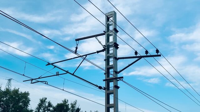 Utility pole against blue sky, birds perched on wires, concrete pylon and insulators under wispy clouds, suburban treeline below, calm atmospheric light, electrical infrastructure