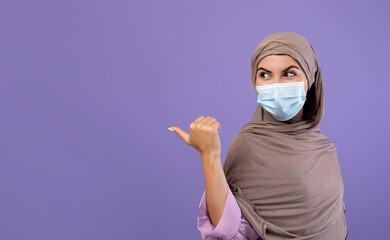 Muslim woman in protective face mask and hijab pointing at copy space for text or advertisement...