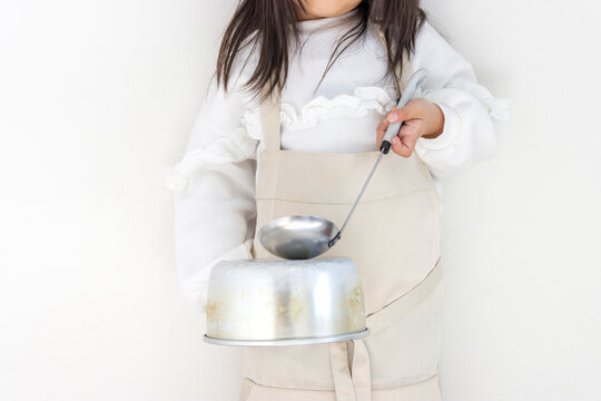 大きなエプロンをだらしなく着た子供が、鍋とお玉で騒音を出している（5歳、女の子、日本人）