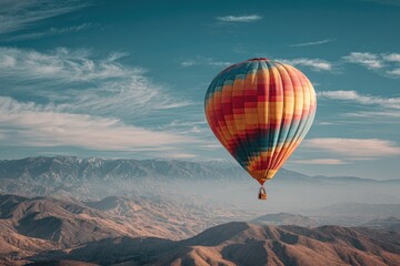 Obraz premium A colorful hot air balloon drifts over a mountainous landscape with a bright, blue sky