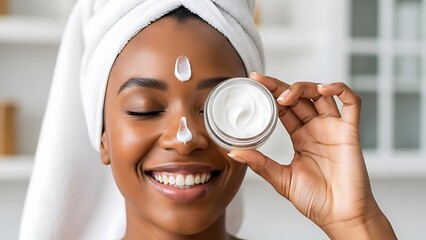 Young Black woman with a towel on her head applying face cream for skincare