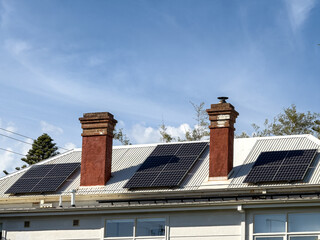 Three solar panels on a white roof with two brick chimneys bright blue sky and sunshine