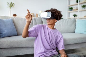 Modern technologies and entertainments. Cool black teen guy in VR headset exploring virtual reality at home, touching imaginary screen, interacting with cyberspace