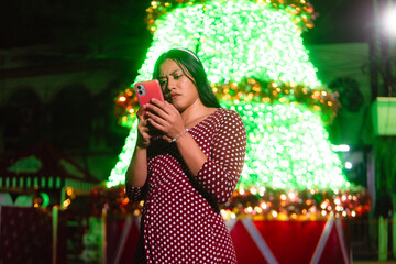 Young latina woman frowning while checking smartphone at park holiday event