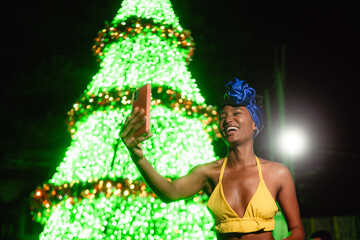 Woman smiling taking selfie near festive christmas tree