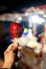 Hand holding candy apple with sprinkles at night fair