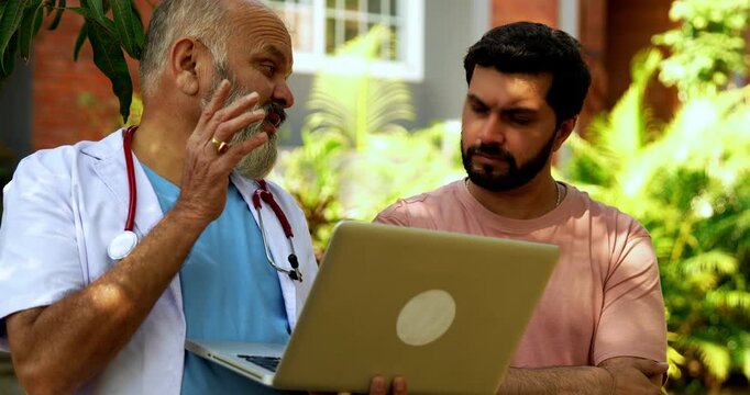 Indian doctor patient discuss case outdoors in natural greenery as senior male physician reviews medical report on laptop or looking at case file with patient during open air healthcare consultation