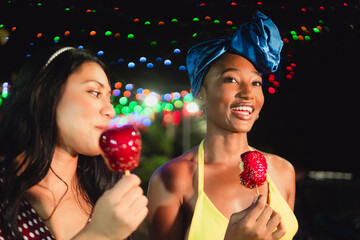 Diverse friends enjoying sweet candy apples at night
