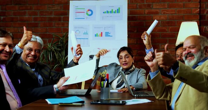 Indian business people celebrating success as senior Indian Asian executives clap and exchange high five to mark achievement during corporate team meeting inside modern office workplace