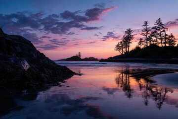 Coastal sunset reflects in wet sand with silhouetted trees and rocky outcroppings