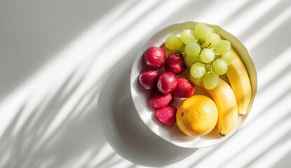 Overhead view of a white bowl filled with assorted fresh fruit, with shadow play