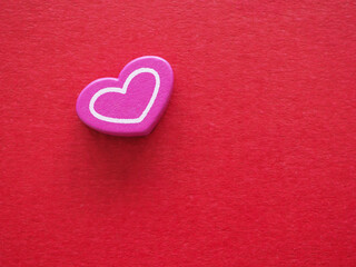 High angle view of a pink wooden heart with white outline on textured red paper background. Minimalist concept for Valentine's Day, love, romantic greeting card and anniversary celebration copy space.