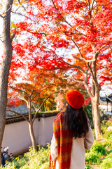 Young female tourist relaxing and enjoying the view of red maple leaves during the autumn foliage season at Suzhou, China