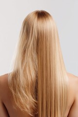 Long, radiant blonde hair showcases stunning shine and smooth texture against a soft, neutral background in a minimalist setting
