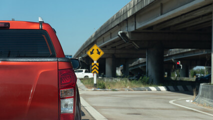 Rear view of a red pickup truck driving on the road under a concrete bridge with a yellow traffic sign indicating a split path. Transportation concept.