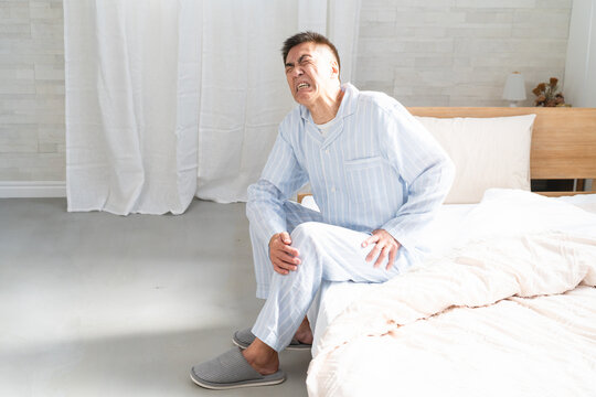 起きてベッドの上で膝の痛みを訴える男性