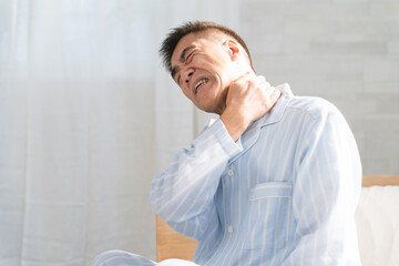 起きてベッドの上で肩を揉む男性 © aijiro