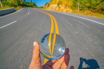 Hand held glass sphere reflecting a mist-covered mountain village and winding road, evoking freedom, inspiration, and a journey into mystery. Crystal Ball Over a Curve Road Leading Into the Mist