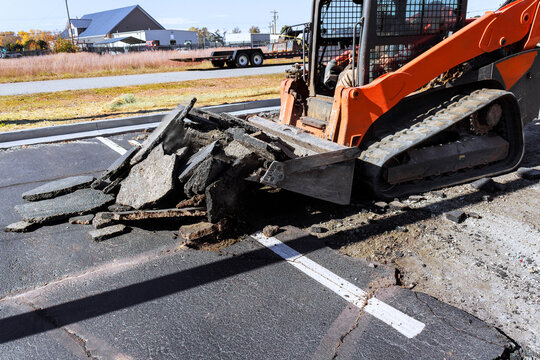 Heavy machinery removes damaged asphalt from parking lot in construction site
