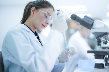Focused female pathologist using a microscope to examine tissue biopsy samples in a sterile hospital laboratory. Professional scientist conducting medical research for disease diagnosis.