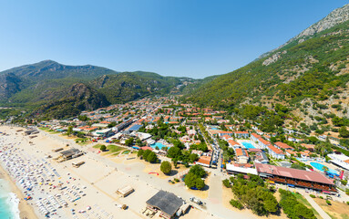 Oludeniz, Turkey. Aerial view of beach with cafe, luxury villas with swimming pools, and forest-covered mountains under summer sun. Aerial view.