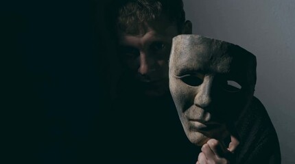 A person holding a mask in a dimly lit room, conveying mystery and secrecy. The lighting casts shadows that deepen the enigmatic atmosphere, with the mask as the focal point