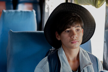 Pensive young male traveler with a backpack and hat, looking up while sitting next to a bus. Focus on the feeling of anticipation, urban travel, and a sense of journey.