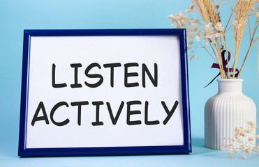 Listen actively symbol. Concept words Listen actively on beautiful wooden picture frame. Beautiful light blue background with flower vase. Business and Listen actively concept. Copy space.