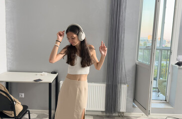 Woman enjoys music and dances inside a room with large windows during sunset