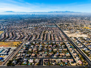 Aerial view of suburban neighborhood meeting desert mountains under clear blue sky, residential development at the edge of Las Vegas