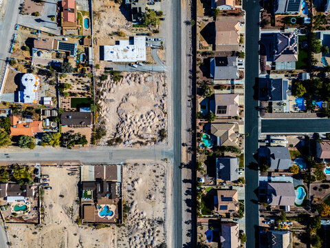 Aerial view of suburban residential neighborhood in Los Angeles desert area with intersecting streets, detached houses, swimming pools, dry landscapes, and low density urban planning seen from directl
