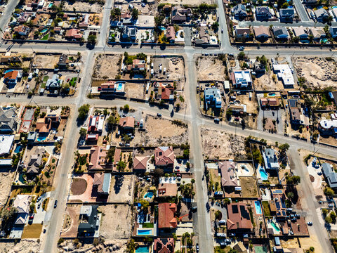 Aerial view of suburban residential neighborhood in Los Angeles desert area with intersecting streets, detached houses, swimming pools, dry landscapes, and low density urban planning seen from directl