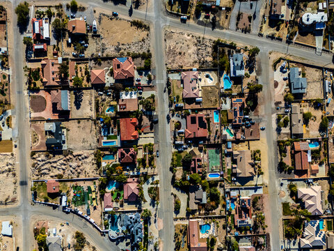 Aerial view of suburban residential neighborhood in Los Angeles desert area with intersecting streets, detached houses, swimming pools, dry landscapes, and low density urban planning seen from directl