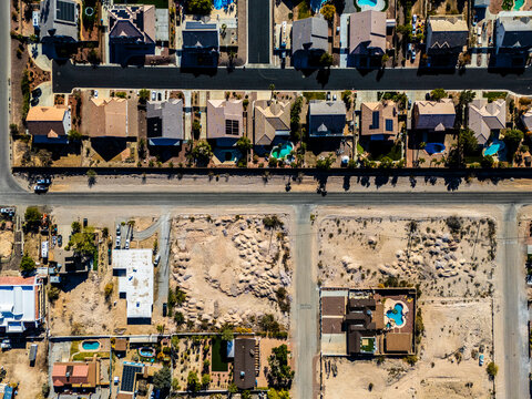 Aerial view of suburban residential neighborhood in Los Angeles desert area with intersecting streets, detached houses, swimming pools, dry landscapes, and low density urban planning seen from directl