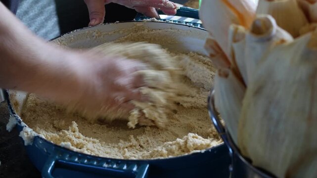 Close-up of a person kneading masa dough in a large bowl to prepare traditional tamales at home