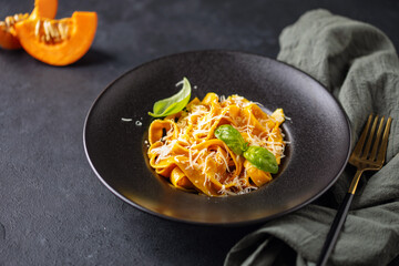 Homemade pumpkin tagliatelle pasta with parmesan cheese in a plate on the table. Italian cuisine