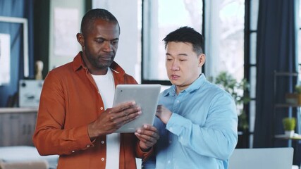 In a contemporary office, two business professionals focus on a digital tablet, sharing ideas and insights. Natural light illuminates the space, enhancing their productive atmosphere.